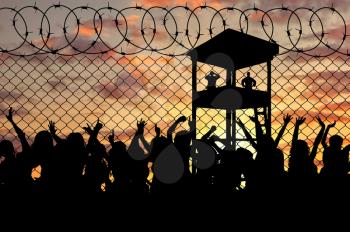 Concept of the refugees. Silhouette of a crowd of refugees at the border against the sunset and the guard tower