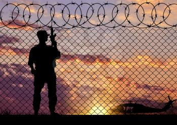 Concept of terrorism. Silhouette of a terrorist near the border fence in the sunset near the helicopter