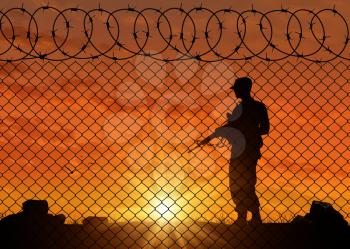 Concept of terrorism. Silhouette of a terrorist near the border fence in the sunset