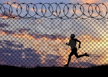 Concept of refugee. Silhouette of running a refugee at the border fence at sunset