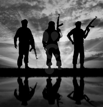  Silhouette of three terrorists with weapons at sunset with reflection in water