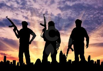 Silhouette of three terrorists with a weapon against a background of a sunset in the city