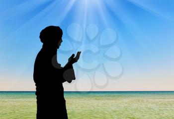 Concept of Islamic culture. Silhouette of man praying on the background of the sea in the rays