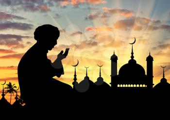 Concept of the Islamic religion. Silhouette of man praying on the background of the town hall at sunset