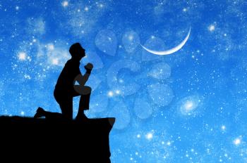 Concept of religion. Silhouette of man praying on the background of the sky with the moon and stars