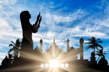 Concept of the Islamic religion. Silhouette of praying woman against the backdrop of the town hall at dawn