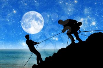 Concept of aid. Silhouette of two climbers helping each other against the backdrop of the sea and the moon at night