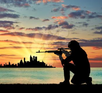 Silhouette of a terrorist with a weapon against a background of a sunset near the town