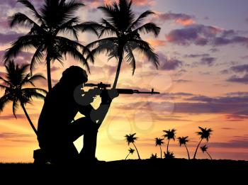 Silhouette of a terrorist with a weapon against a background of a sunset with palm trees