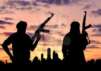 Silhouette of two terrorists with a weapon against a background of a sunset in the city