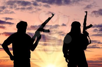Silhouette of two terrorists with a weapon against a background of a sunset 
