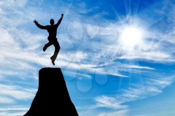 Silhouette of businessman jumping at the peak of the mountain on the background of the sunny sky
