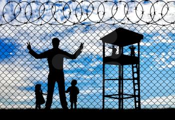 Concept of the refugees. Silhouette refugees father and two hungry children on the background of the fence and watchtower