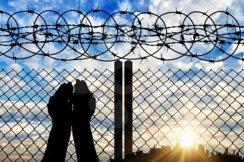 Concept of religion. Silhouette of hands facing the sky against a background of a fence with barbed wire and the city in the distance