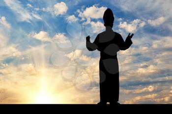 Concept of religion. Silhouette of the Pope against the evening sky in the rays of light