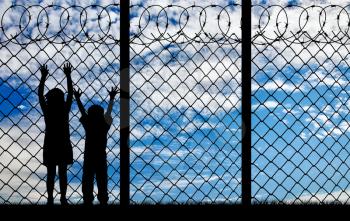 Concept of refugee. Silhouette hungry refugee children near the fence with barbed wire