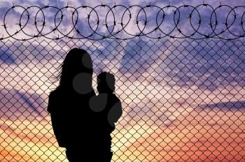Concept of the refugees. Silhouette mother with child refugees near the fence at sunset