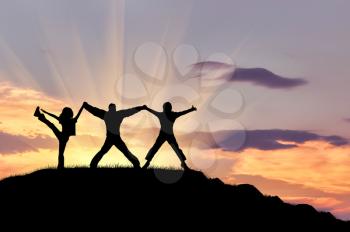 Concept of success. Silhouette of three happy people on top of the mountain against the evening sky