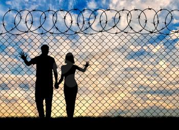 Concept of the refugees. Silhouette of refugee families near the fence at sunset