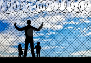 Concept of the refugees. Silhouette refugees father and two hungry children on the background of the fence