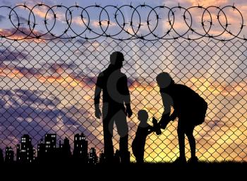 Concept of the family of refugees. Silhouette of refugee families near the fence on the border on the background of the city in the distance at sunset
