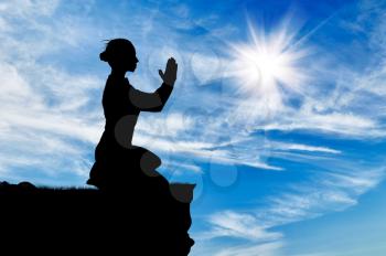 Silhouette of praying woman on top against cloudy sky