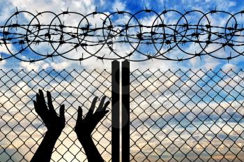 Concept of religion is Islam. Silhouette of hands facing the sky against a background of a fence with barbed wire 