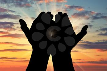 ?oncept of Islam, the Koran. Silhouette of praying hands facing the sky at sunset
