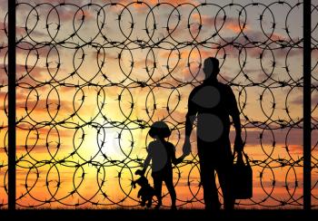 Concept of refugee. Silhouette of a family with a child refugee father near the fence with barbed wire at sunset