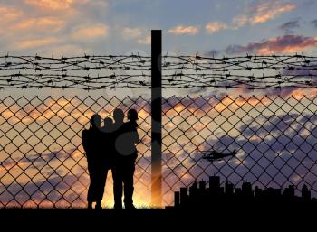 Silhouette of a family with children of refugees and fence with barbed wire on the background of evening city away