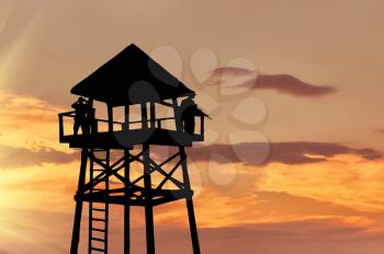 Concept of security. Silhouette of a watchtower with soldiers at sunset