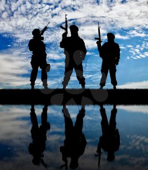Concept of a terrorist. Silhouette of terrorists with a rifle and a reflection on the water against the background of dawn