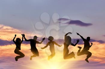 Concept of emotion. Silhouette of a happy group of people jumping at sunset