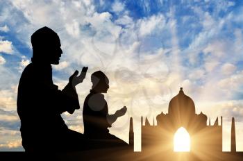 The concept of religion Islam. Silhouette of two men praying at sunset in the background Mosque