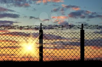 Boundary. Silhouette of iron fence with barbed wire on the background of sunset