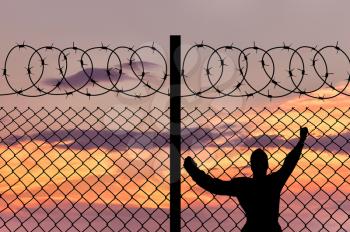 Concept of security. Silhouette of refugee men and metal fence with barbed wire on the background of the beautiful sky