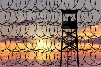 The concept of security. Silhouette of the observation tower on the background of the fence with barbed wire at sunset