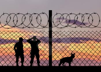 Concept of security. Silhouette of the military with a dog on the background of the fence with barbed wire at sunset