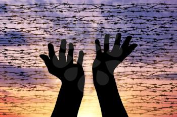Concept of the religion of refugees. Silhouette outstretched arms to the sky against a background of barbed wire at sunset