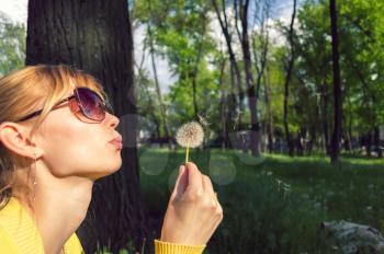 leisure and recreation concept. Young woman blowing on a dandelion in the forest