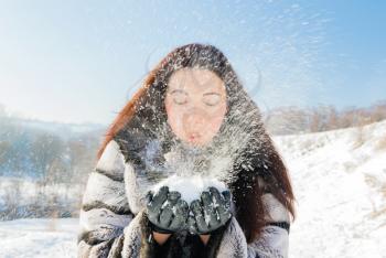 Happiness emotions concept. Young woman blowing in the snow in her hands