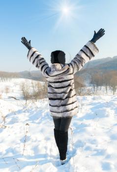 Happiness emotions concept. Happy woman in a fur coat standing on top of a hill in winter