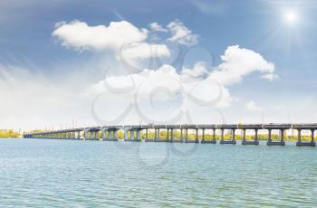  Long concrete bridge across the river against the backdrop of a cloudy sky