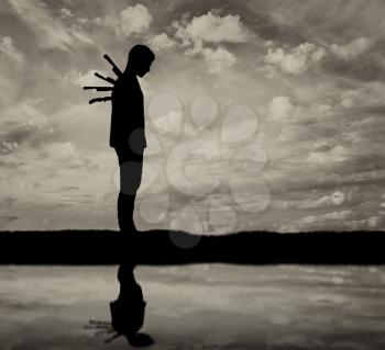Betrayal and treachery concept. Silhouette of a sad man with a knives in back and reflected in water