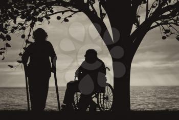 Disabled persons in wheelchair and on crutches under tree near sea. Concept of disability