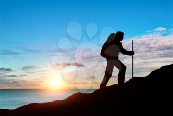 Ascent climber on top of a mountain on a background of sea sunset. Concept of challenge