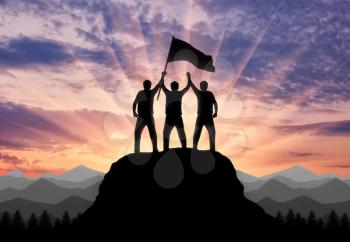 Silhouette of two climbers on a mountain top with a flag in his hand. Concept of a business team