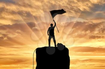 Silhouette of a climber on a mountain top with a flag in his hand. Concept of success and motivation