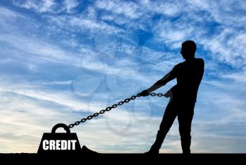 Silhouette of a man chained to a heavy load under the name of the credit. He drags him hard. The concept of high risk in taking a loan