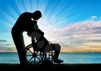 Silhouette of a man kissing a disabled woman in a wheelchair by the sea. The concept of a person with a disability in the family